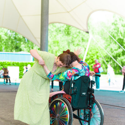 Eine Person im Rollstuhl tanzt eng umschlungen mit einer anderen Person in einem grünen Kleid