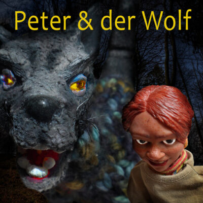 Zwei Puppen nebeneinander: ein Wolf und ein kleiner Junge mit roten Haaren, darüber der gelbe Schriftzug "Peter & der Wolf"